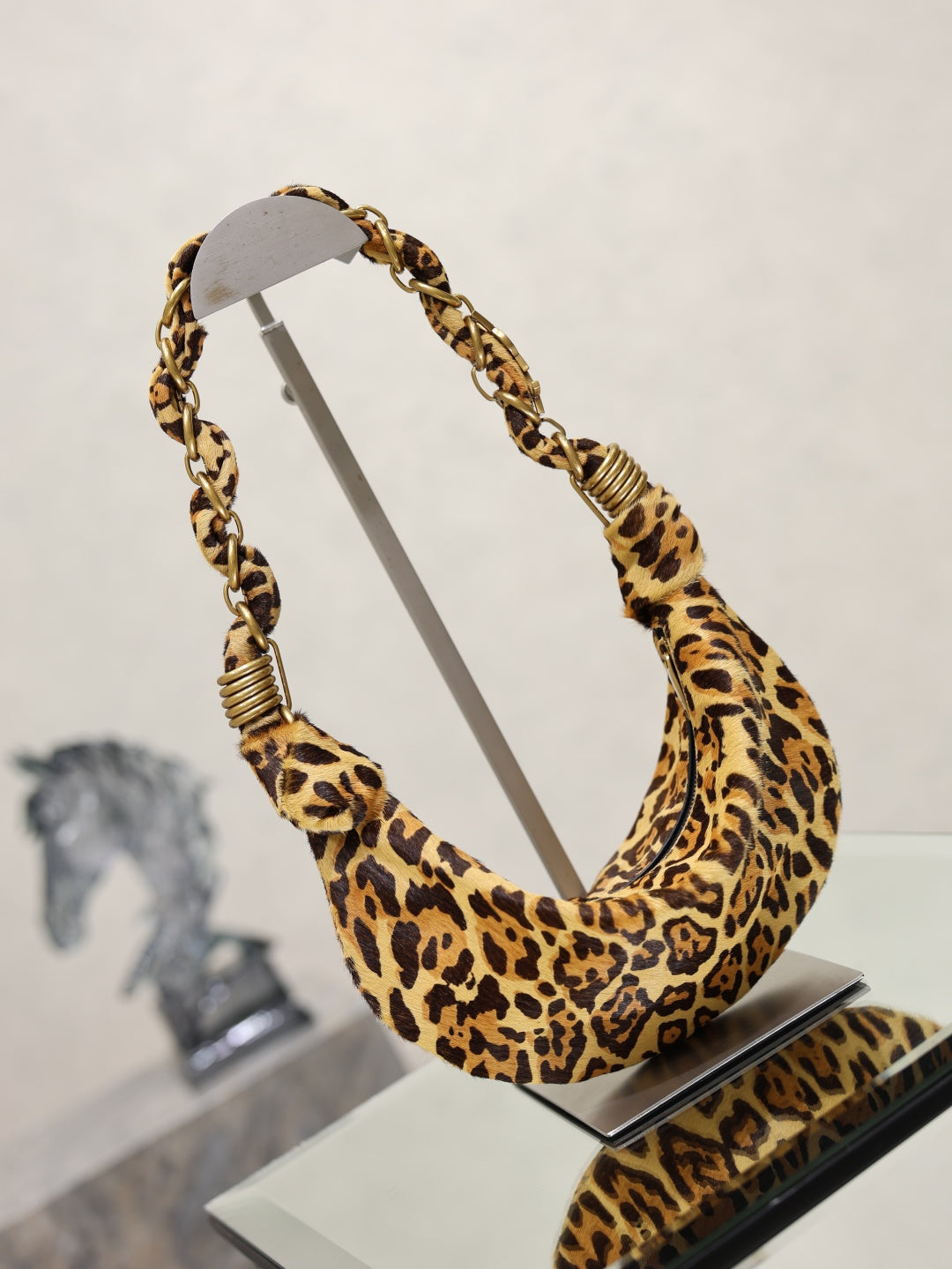 YSL bag on display, leopard-print fabric with braided chain shoulder strap and gold rings