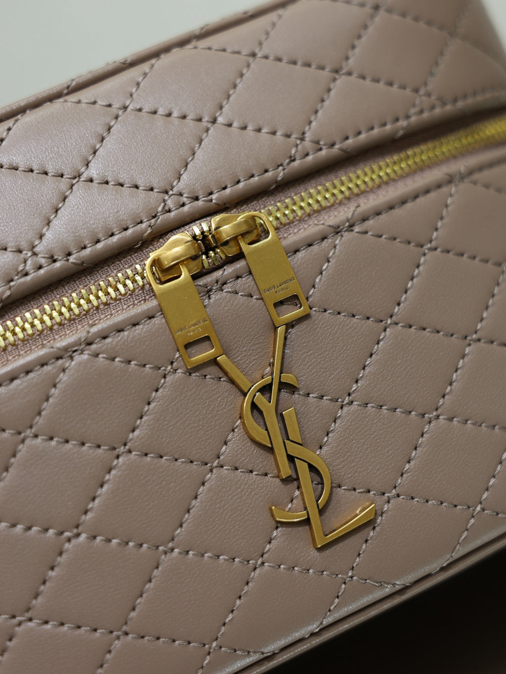 Taupe quilted mini bag close-up of YSL logo on gold-tone zipper pull.