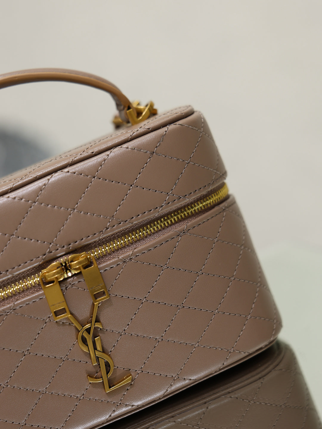 Taupe quilted mini bag close-up of top zip and gold-tone clasp hardware.