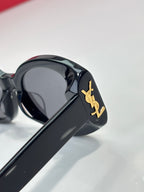 Black cat-eye sunglasses close-up with gold YSL logo and dark tinted lenses