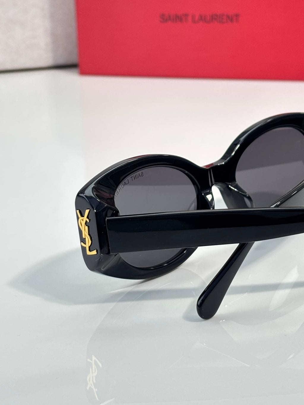 Cat-eye sunglasses with black frames and dark lenses, gold logo near the hinge