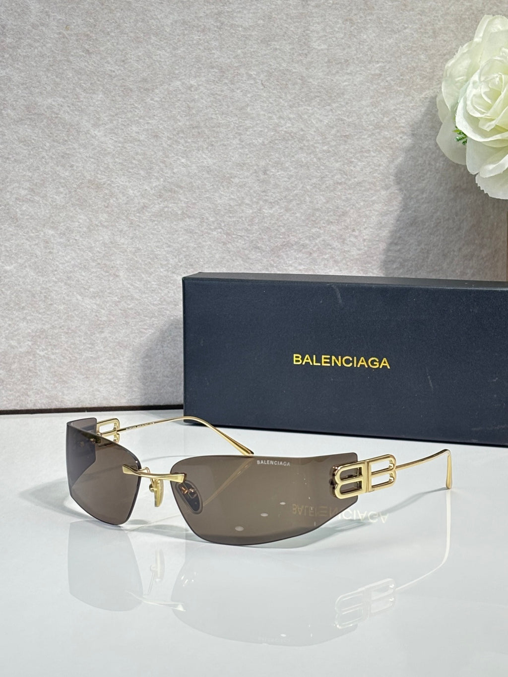 Balenciaga sunglasses with dark taupe lenses and gold-tone frame, bold logo centerpiece