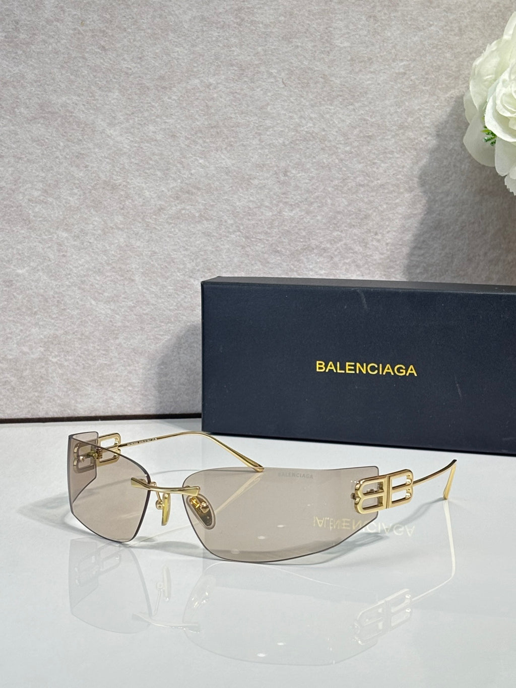 Balenciaga sunglasses with light brown lenses and gold-tone frame, bold logo on temples