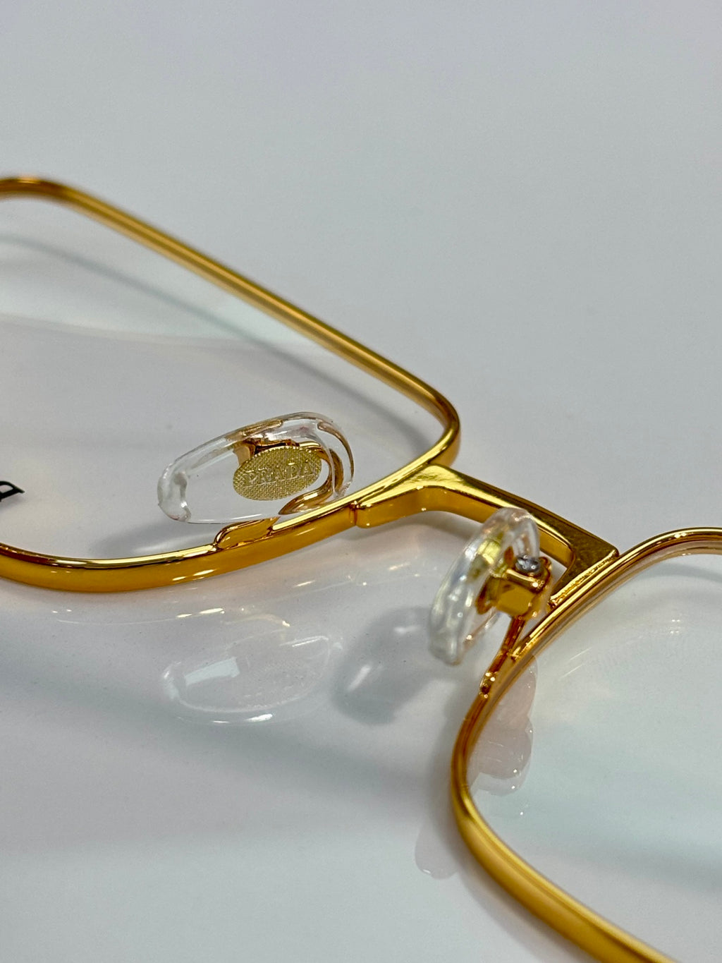 Prada gold eyeglasses close-up of frame arm and lens detail.