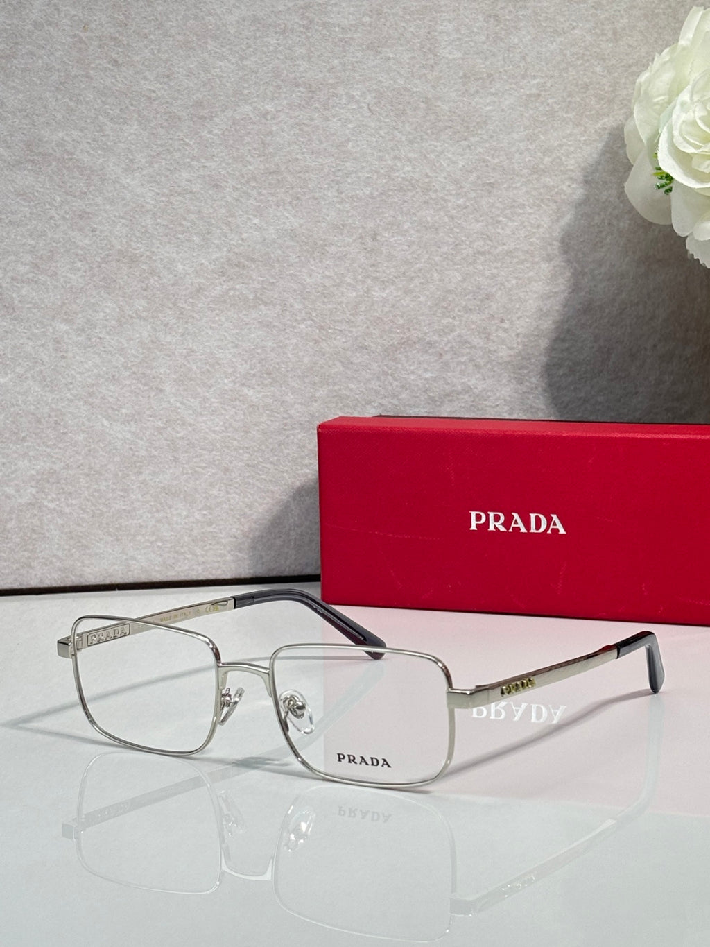 Prada rectangular eyeglasses with clear lenses and silver frame arms.
