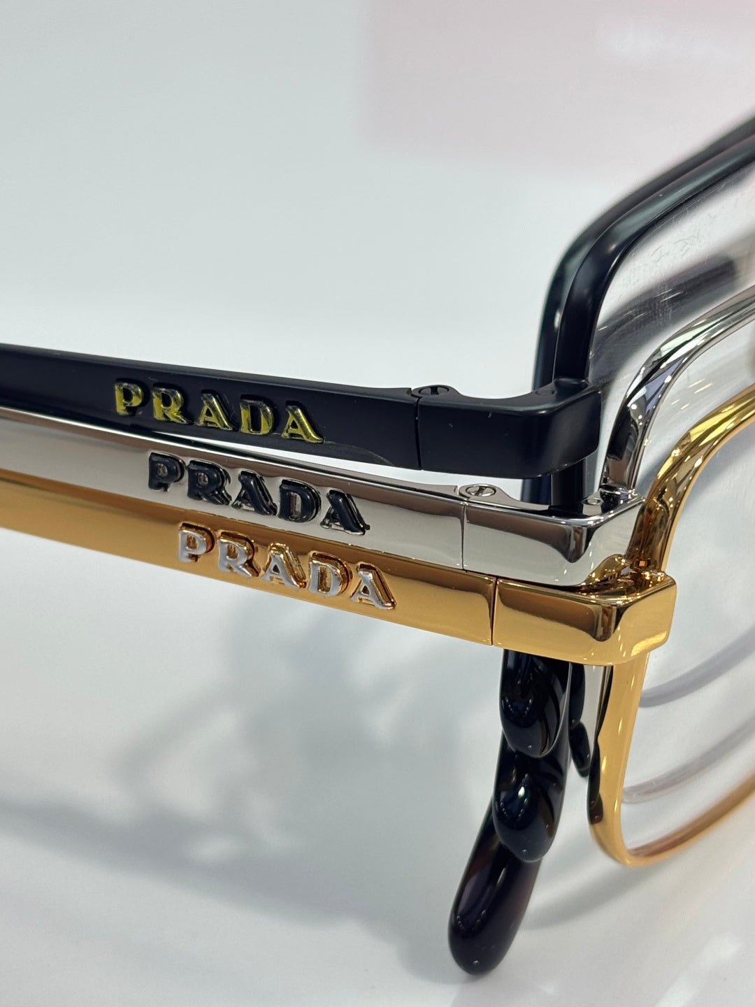 Prada eyeglasses close-up of hinge and gold bridge over clear lens.