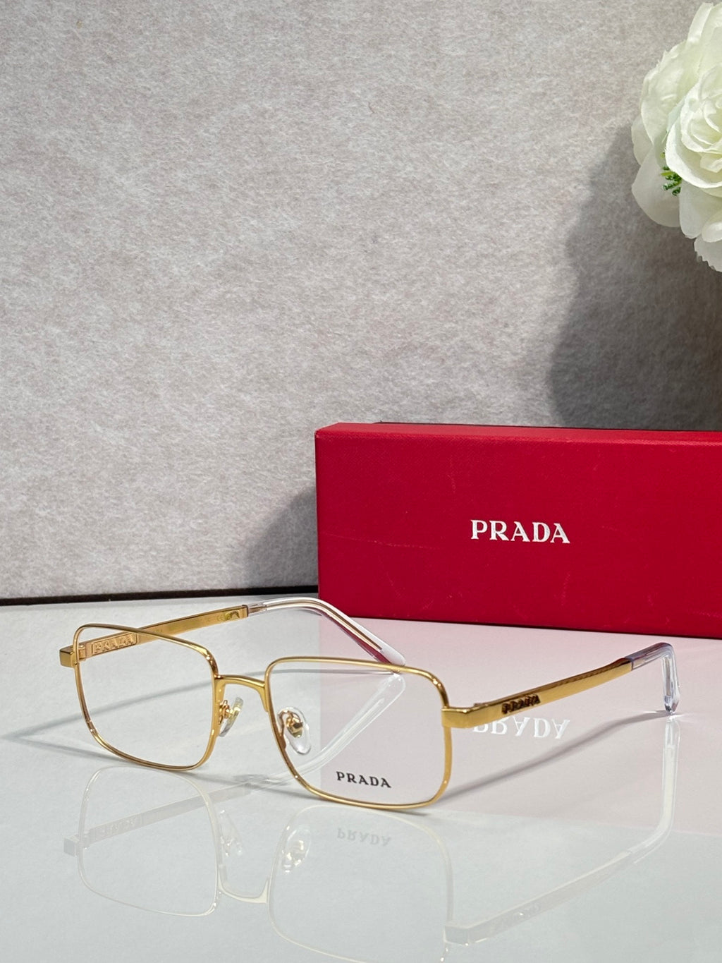 Prada rectangular eyeglasses with gold frame and clear lenses, side profile.