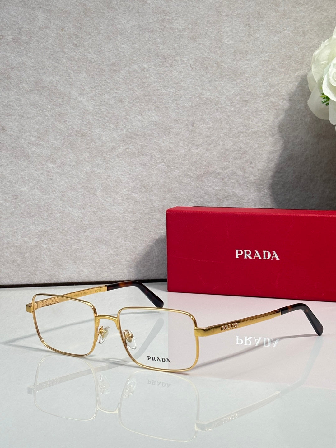 Prada rectangular eyeglasses with gold frame and clear lenses, front-left view.