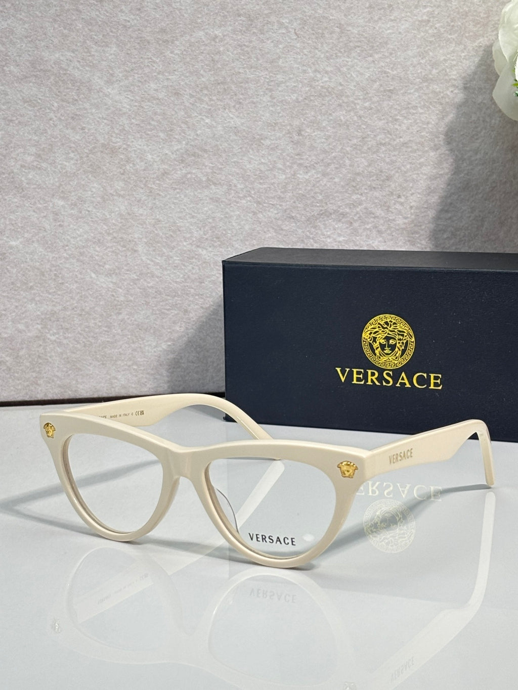 Versace optical glasses, white frame with gold logo accents, clear lenses.