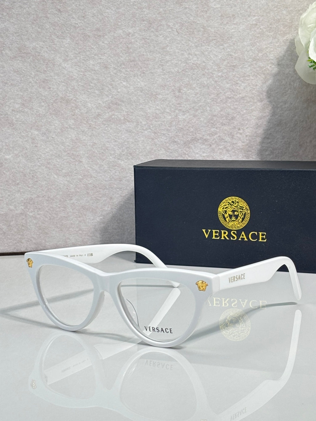 Versace optical glasses, white frame with gold logo details, clear lenses.
