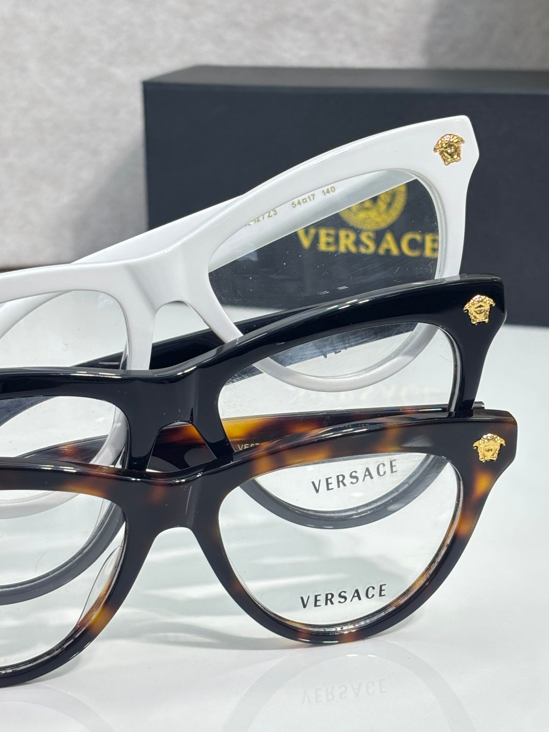 Versace optical glasses, white and tortoiseshell frames with gold logo accents, clear lenses.