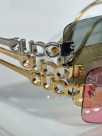 Sunglasses close-up: gold temple with Gucci lettering and pink-tinted lens edge