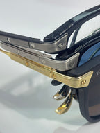 Close-up of navy eyeglass frame with gold-tone hinges and engraved metal temple details.
