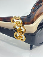 Gucci sunglasses side detail with cream temple, gold chain-style logo, and dark lenses