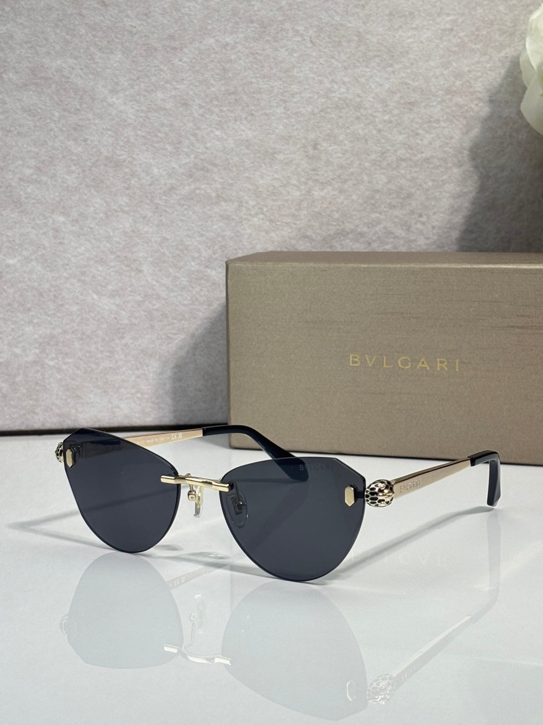 Sunglasses with dark blue lenses, slim black frame, and gold bridge hardware