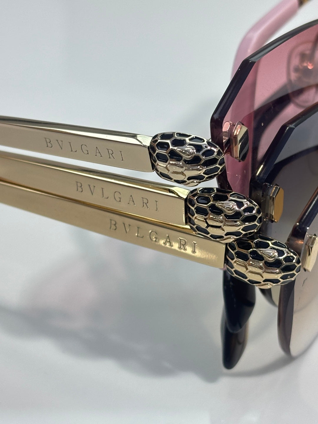 Sunglasses close-up: gold top emblem detail on dark frame with pink lens