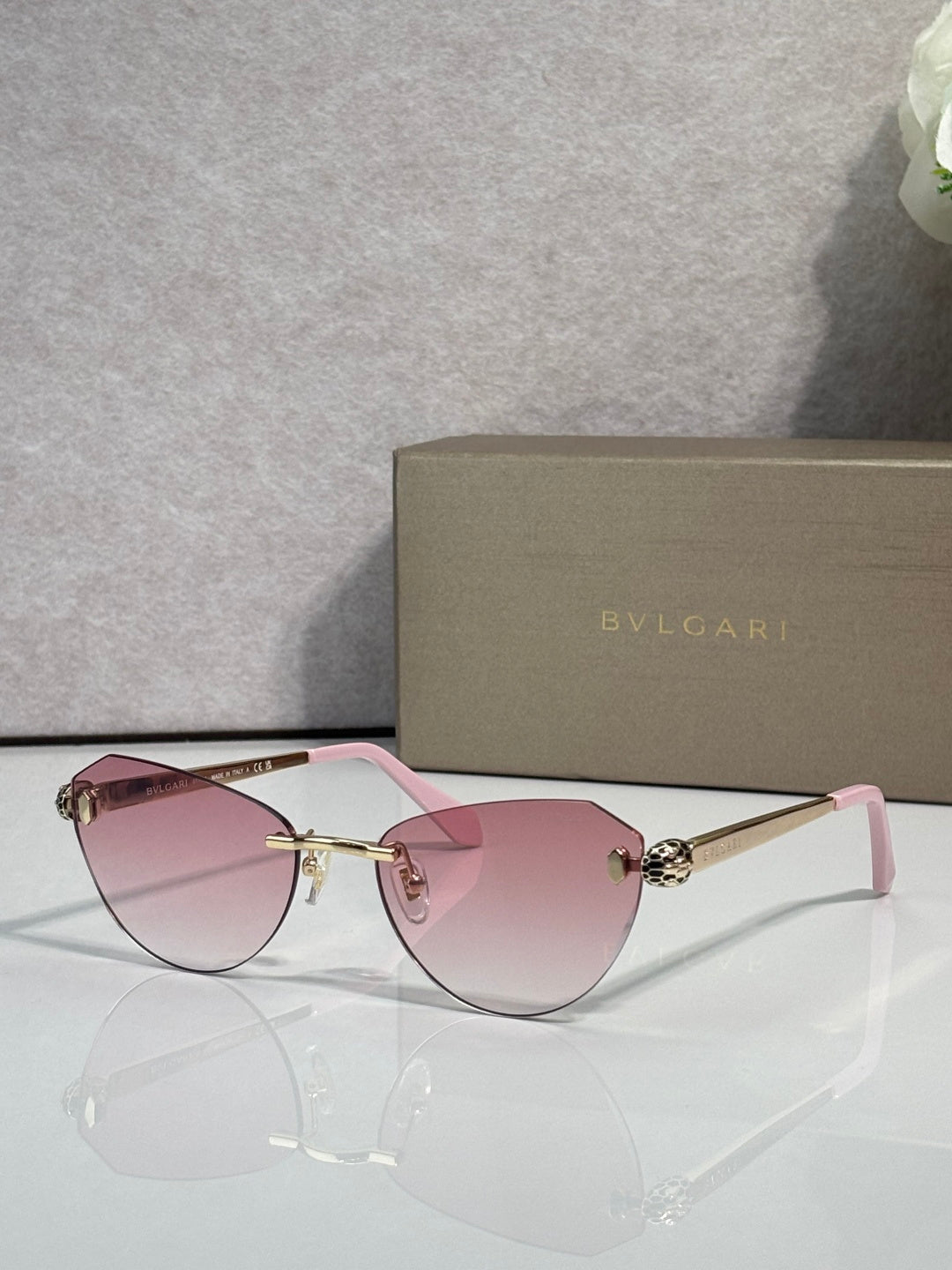 Sunglasses with pink tinted lenses, black frame, and gold metal bridge
