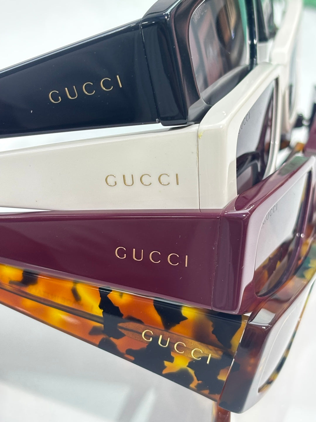 Gucci sunglasses stack showing white, maroon, and tortoise frames with dark lenses