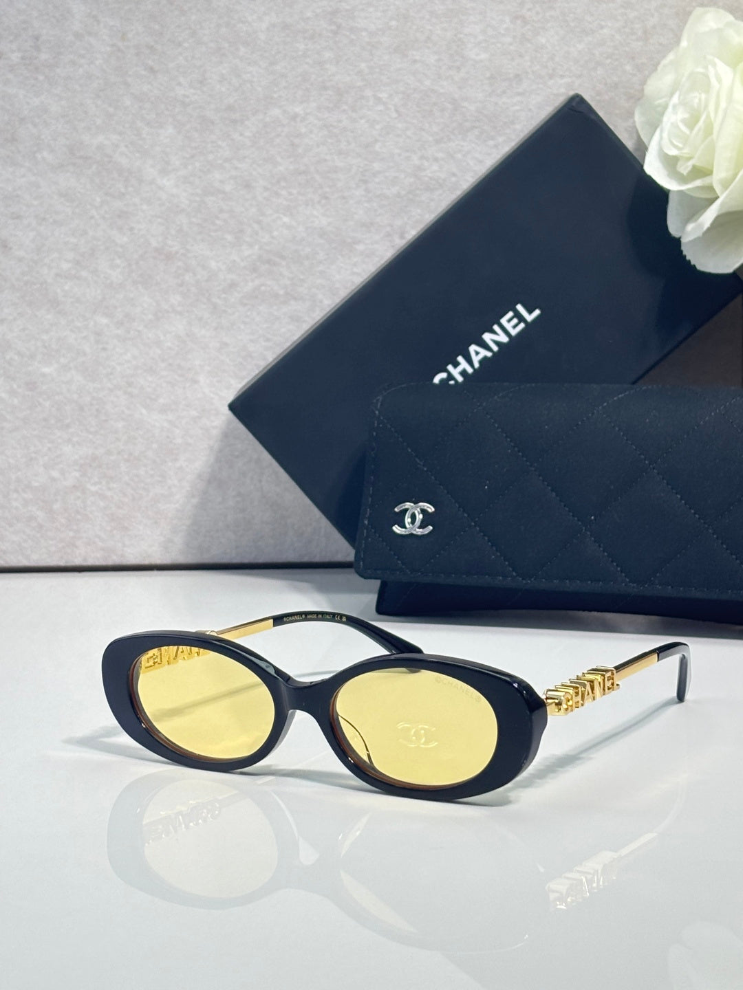 Chanel glasses with dark blue oval frames, yellow-tinted lenses, and gold logo temples.