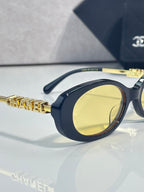 Chanel glasses with navy oval frame, yellow-tinted lens, and gold logo temple detail.