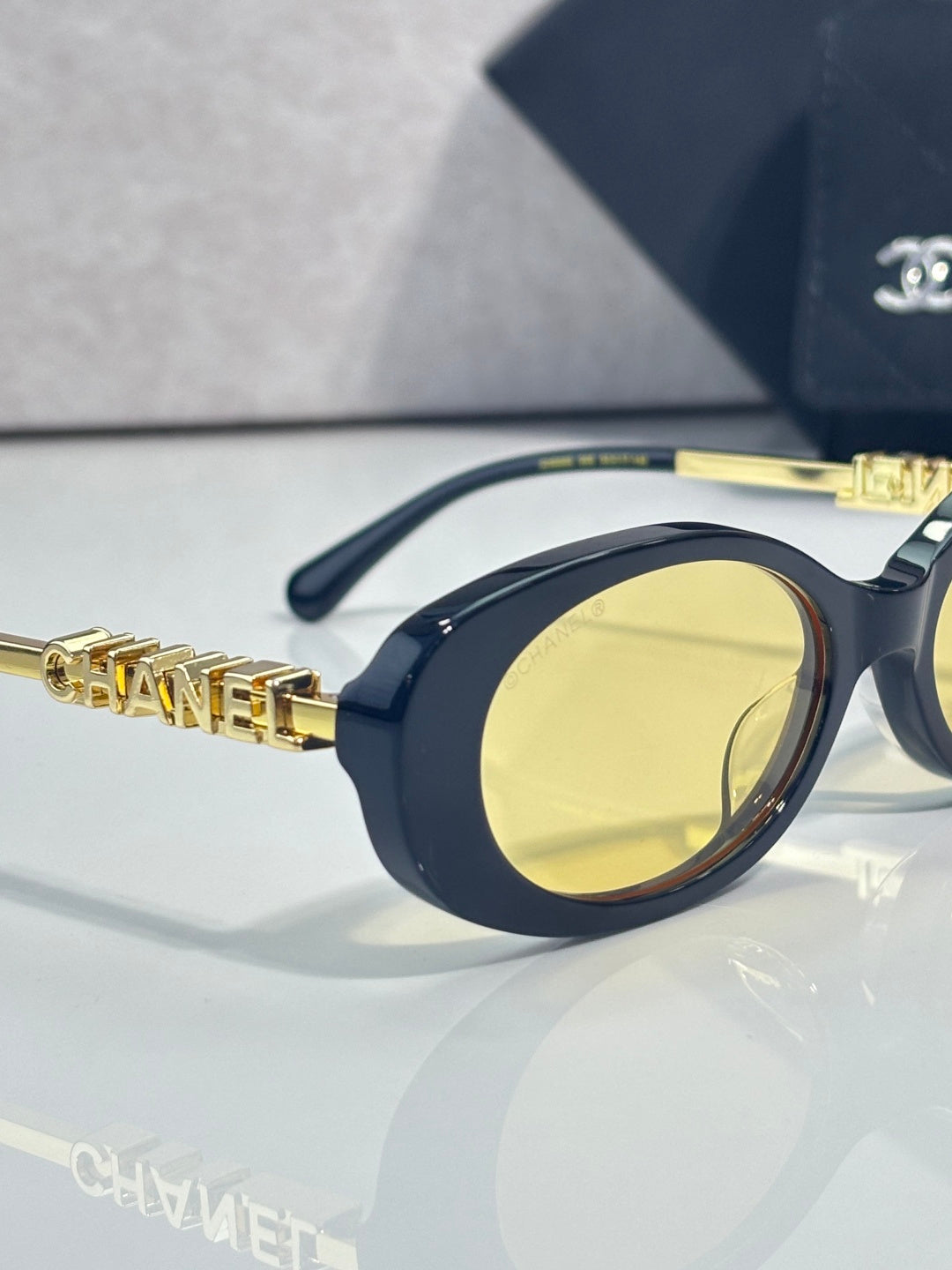 Chanel glasses with navy oval frame, yellow-tinted lens, and gold logo temple detail.