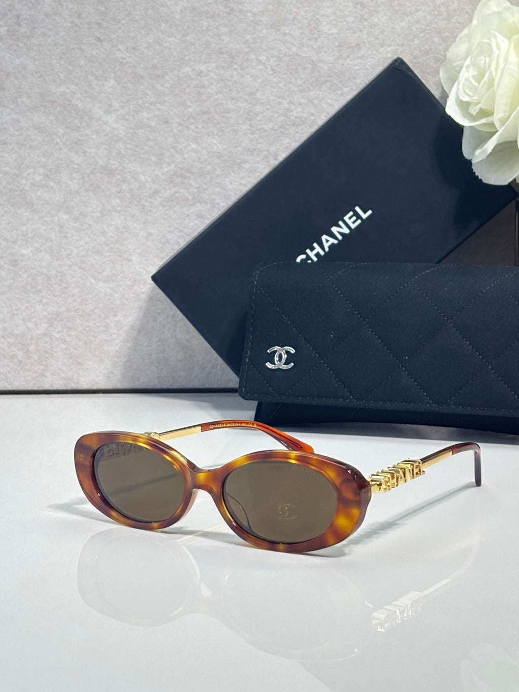 Chanel glasses with tortoiseshell oval frames, dark lenses, and gold logo temple accents.