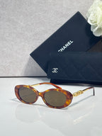 Chanel glasses with tortoiseshell oval frames, dark lenses, and gold logo temple accents.