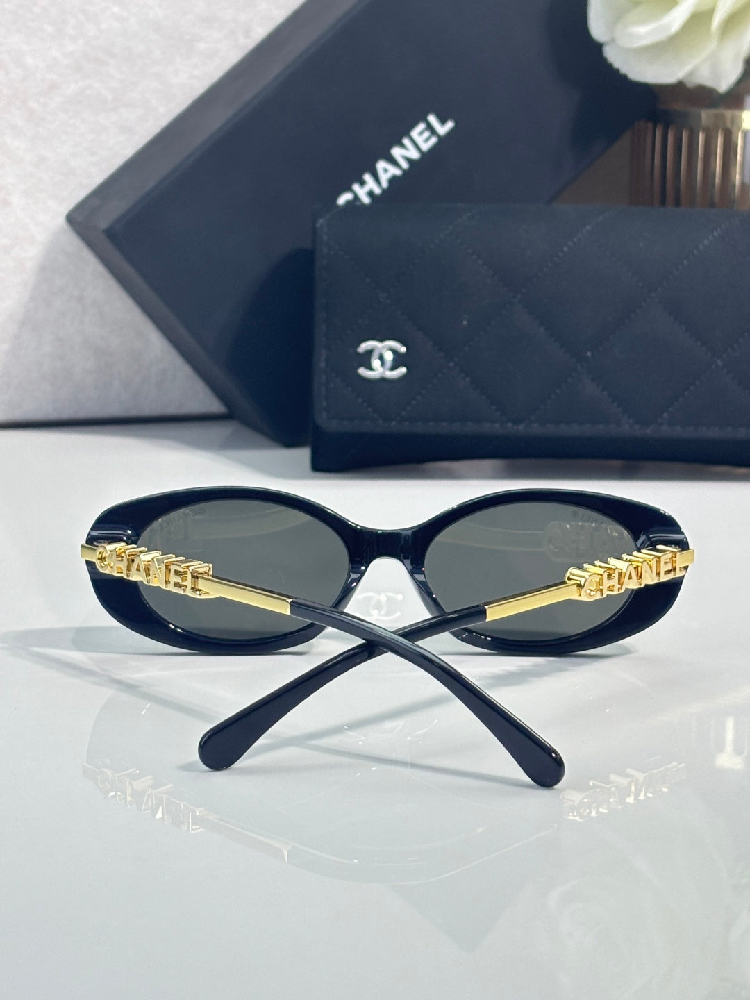 Chanel sunglasses with gold temple branding, resting on navy quilted logo case