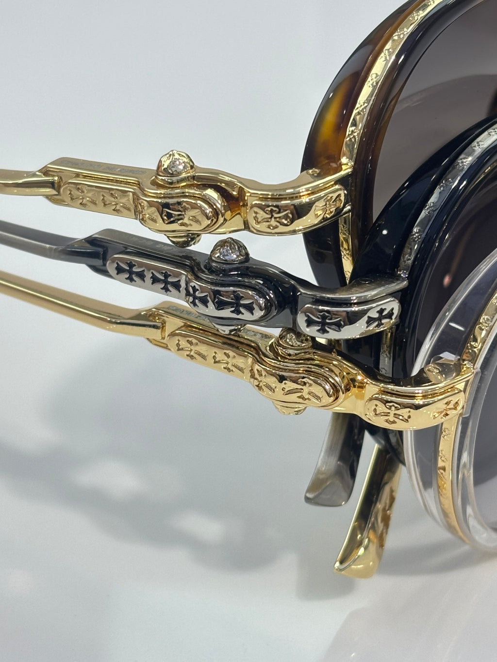 Chrome glasses close-up: ornate gold-and-dark hinge with lens frame edge