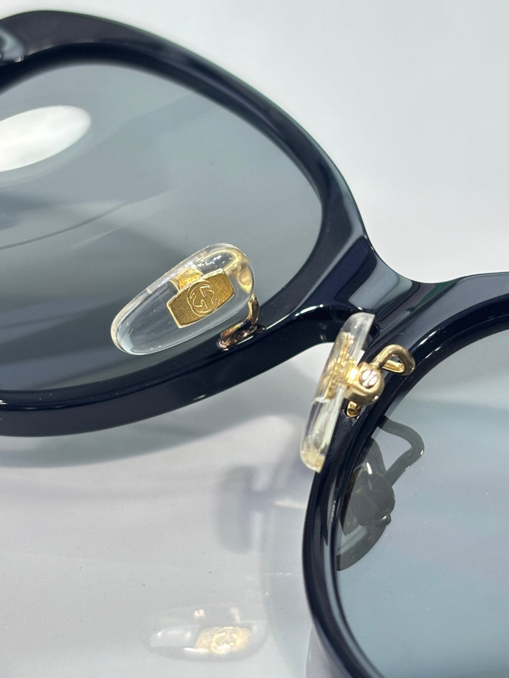 Gucci glasses close-up: dark frame with gold logo plaque on the temple and clear hinge detail.