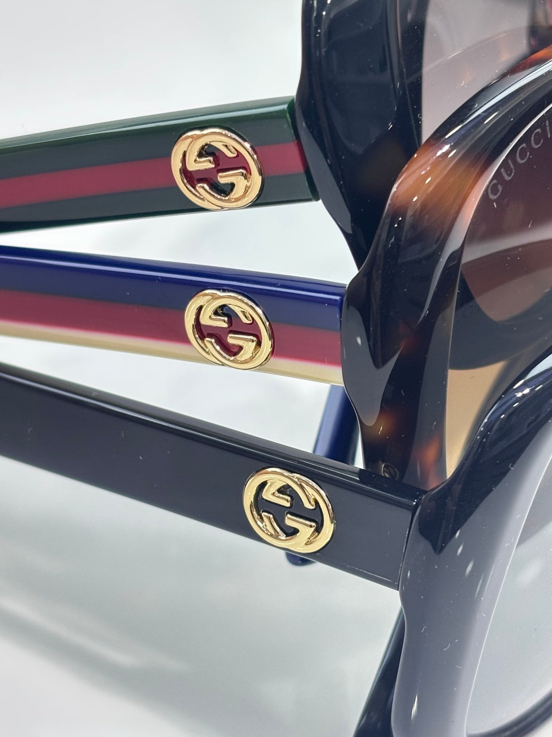 Gucci glasses close-up: gold double-G emblems on the striped temple arms (green, red, blue).