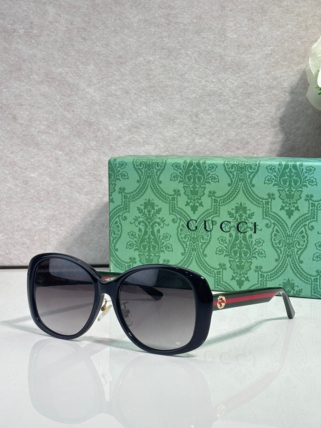 Gucci glasses with dark cat-eye frames, tinted lenses, and green-striped temple accents.