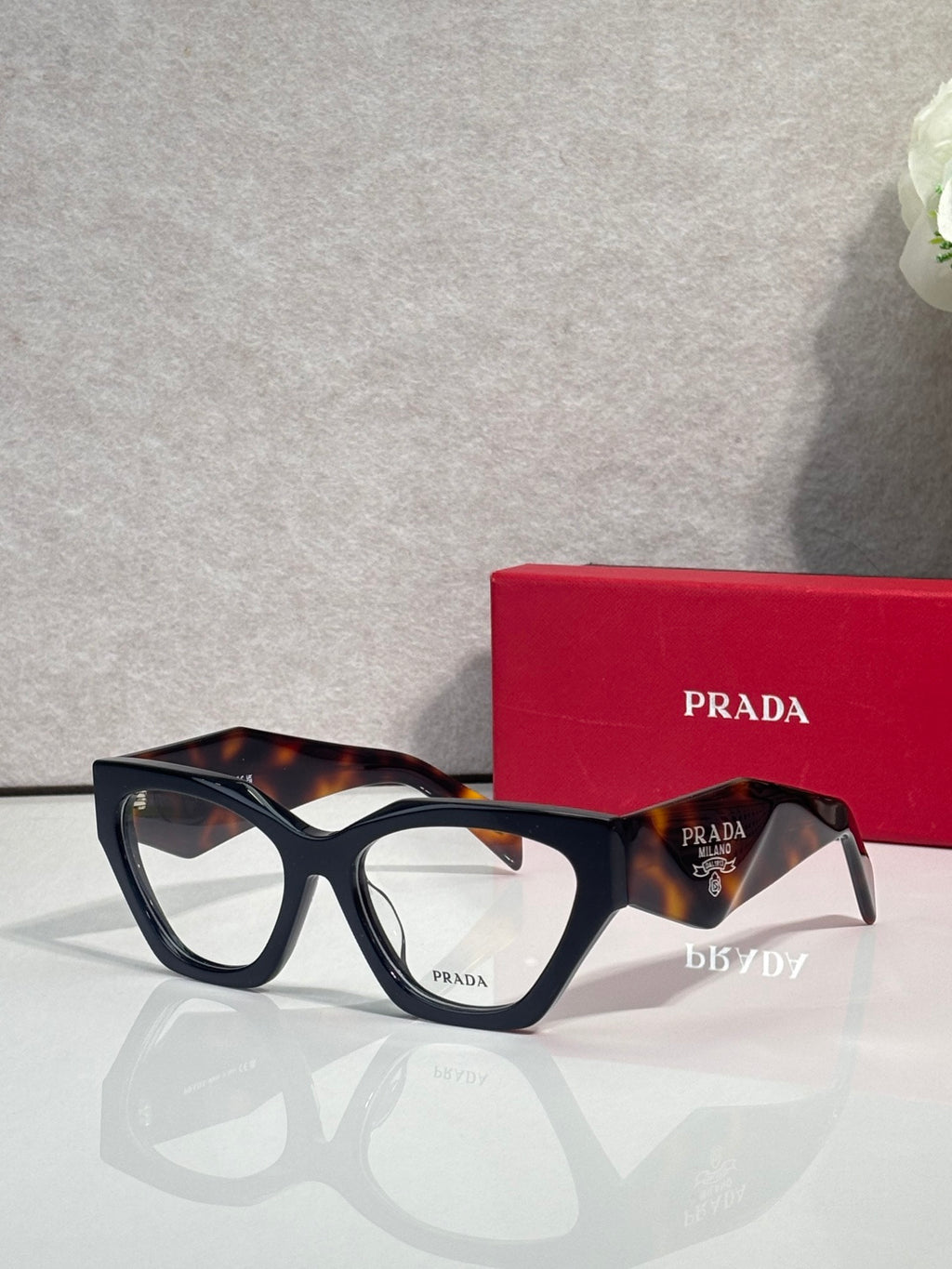 Black square eyeglasses with tortoiseshell arms and clear lenses, Prada branding on front