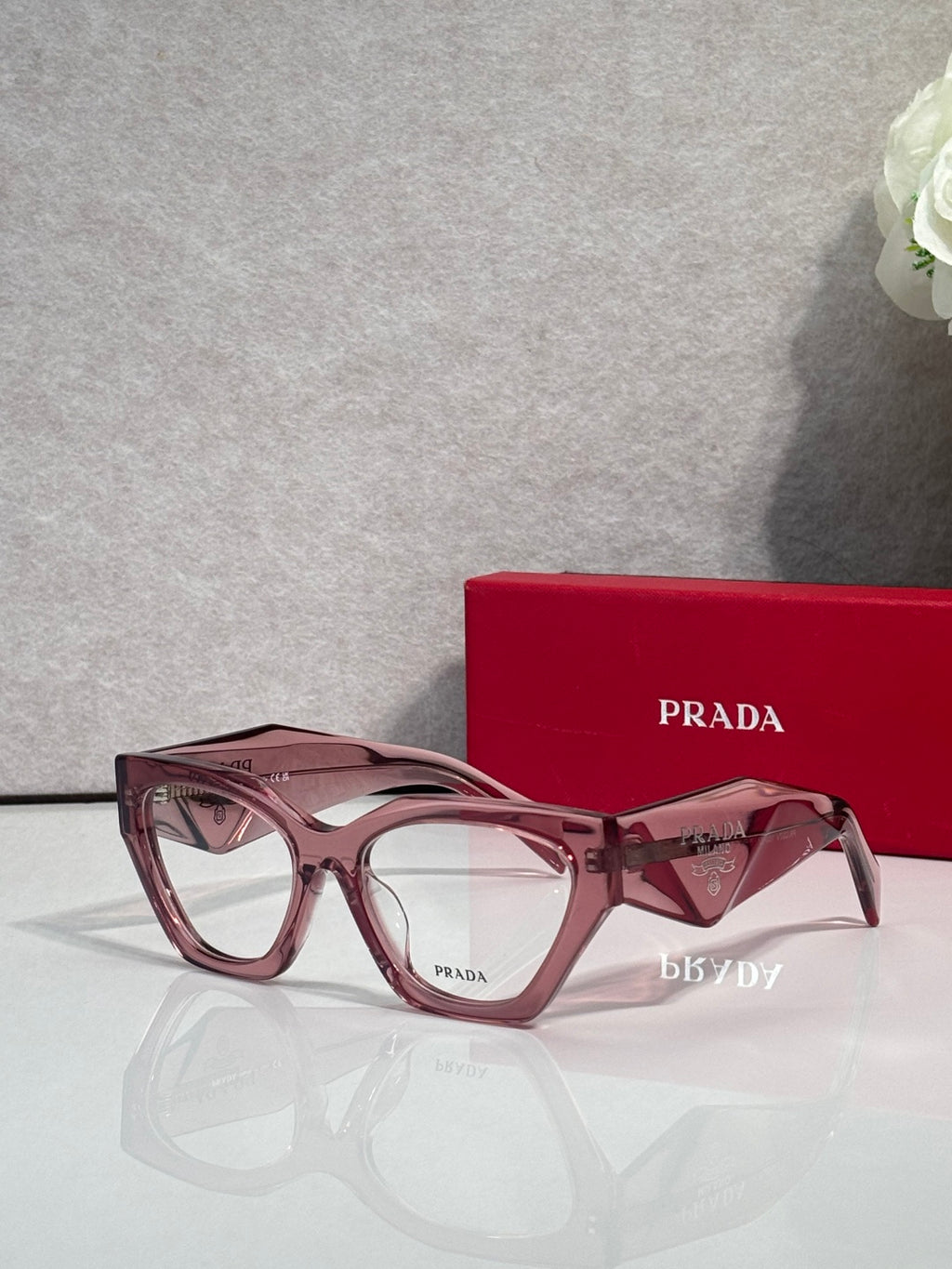 Pink square eyeglasses with translucent arms and clear lenses, Prada logo