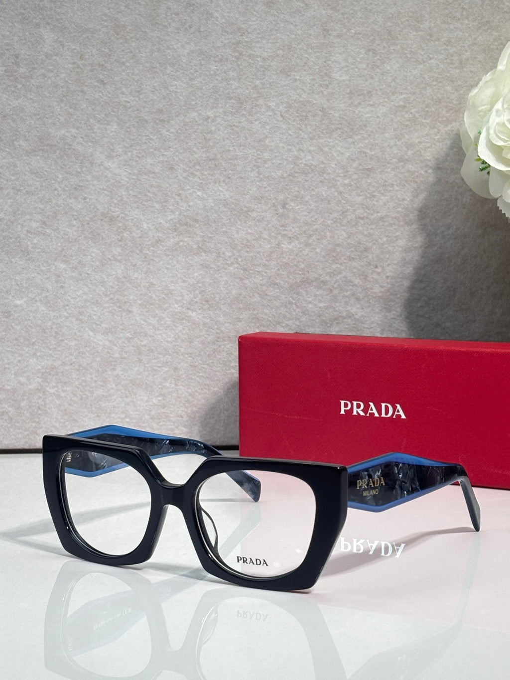 Square navy eyeglasses with blue temple accents and Prada logo on lens