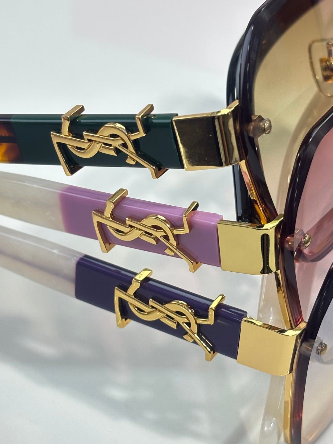YSL glasses close-up: gold YSL logo hinge on purple and navy temples