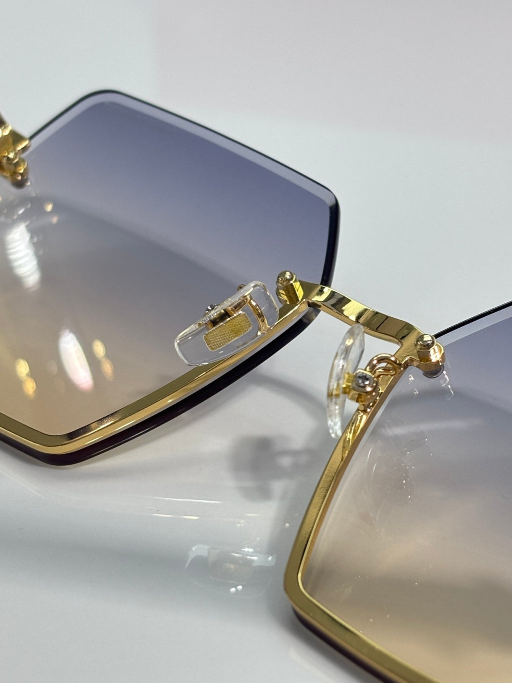 Close-up of square sunglasses frame with gold hinges and dark gradient lens