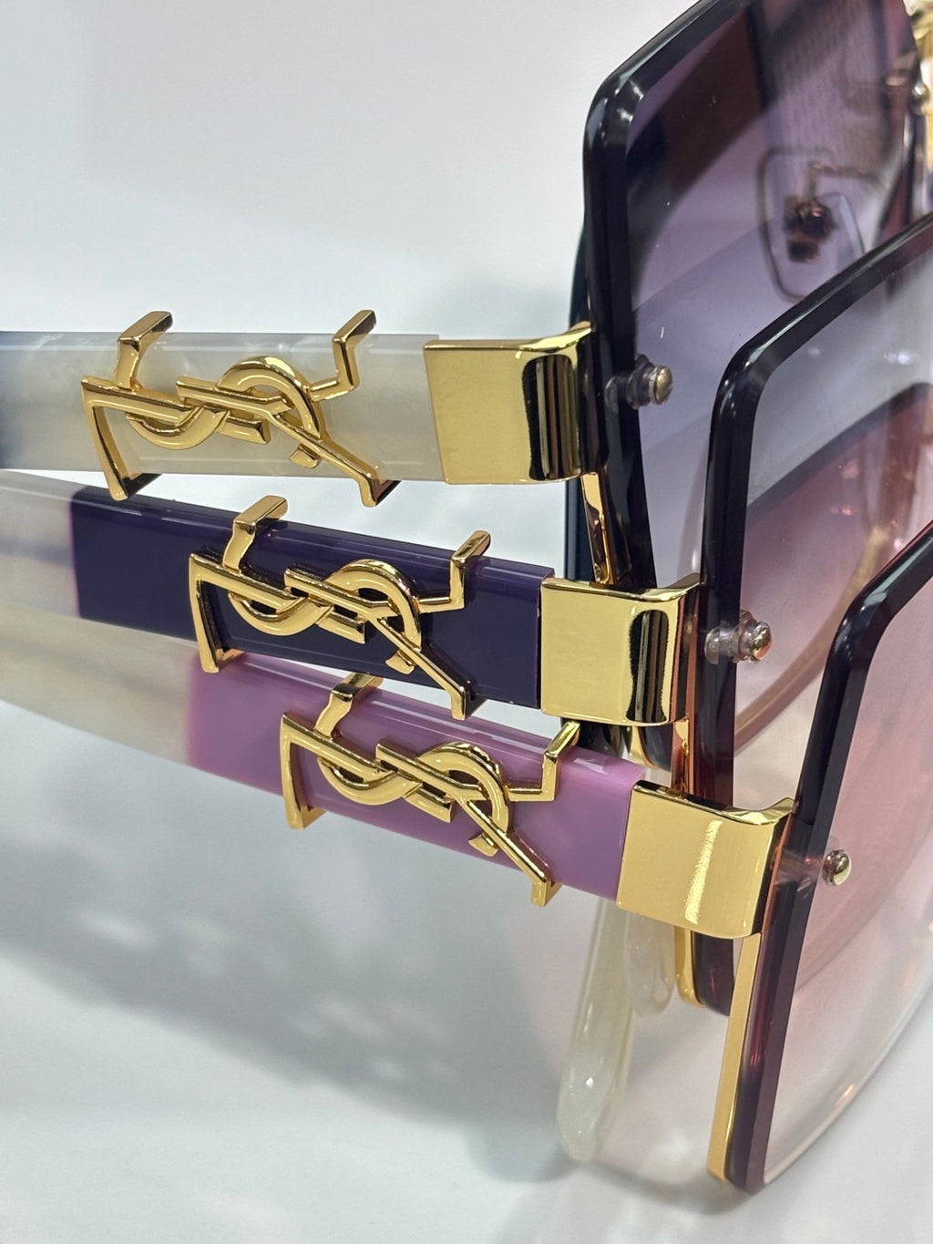 Close-up of square sunglasses with gold YSL hardware and purple gradient lens