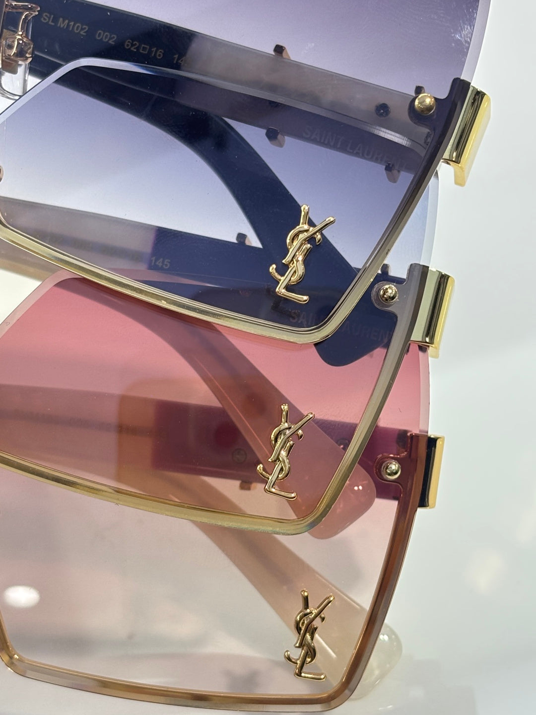 Close-up of rectangular sunglasses with navy gradient lens and gold YSL logo frame