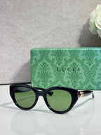Gucci cat-eye sunglasses, black frame with green tinted lenses.