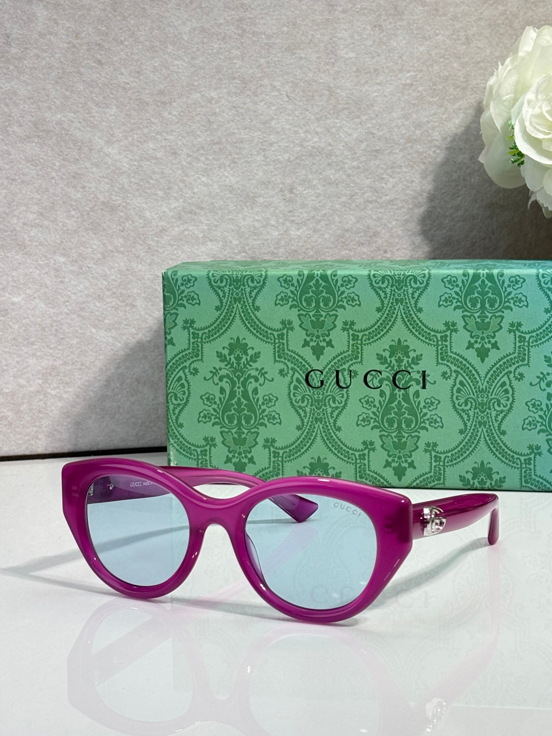 Gucci cat-eye sunglasses, magenta frame with light blue lenses.