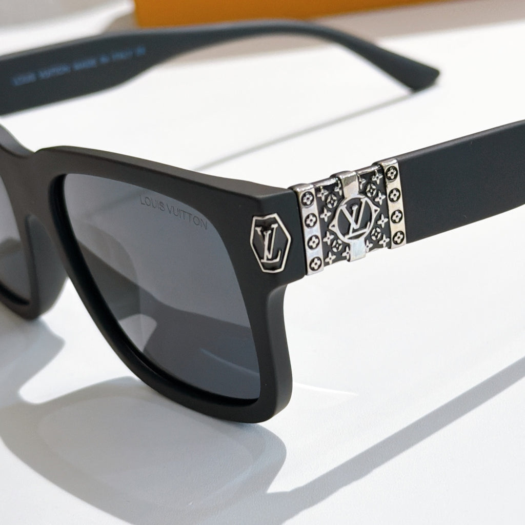 Louis Vuitton sunglasses close-up: patterned temple band with shield logo, black frame.