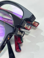 Close-up eyeglasses hinge with black frame, burgundy arm tip, and lens edge