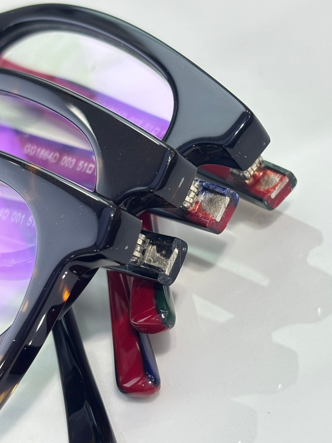 Close-up eyeglasses hinge with black frame, burgundy arm tip, and lens edge