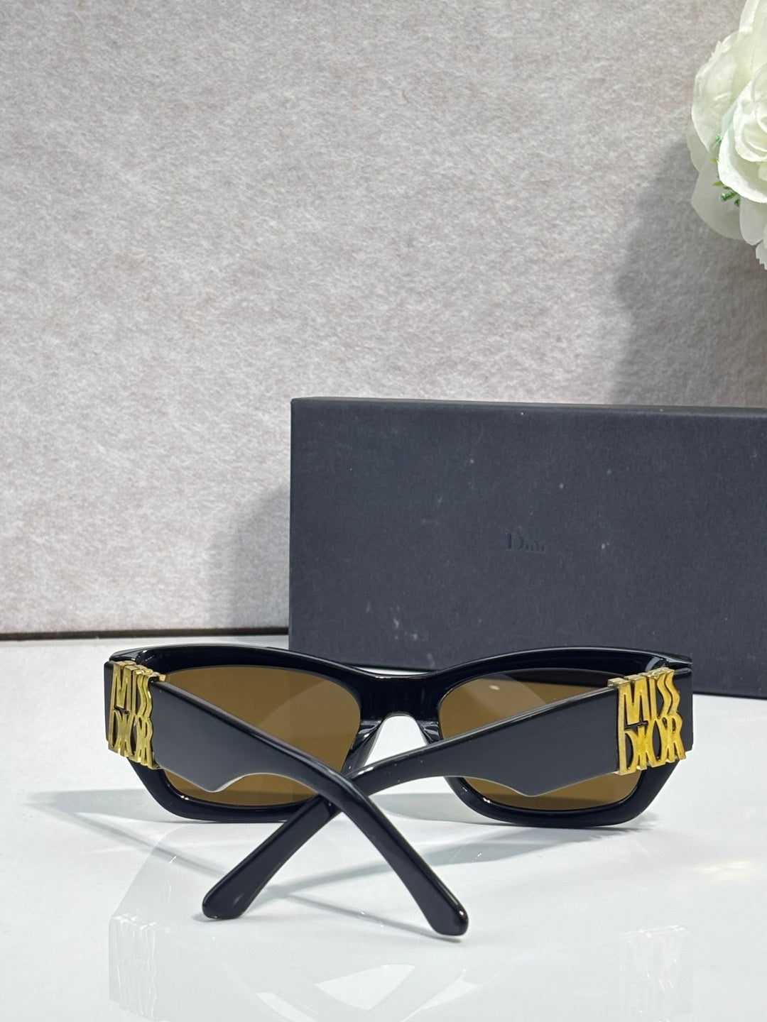 Sunglasses front view with dark navy square frames and gold logo on both temples