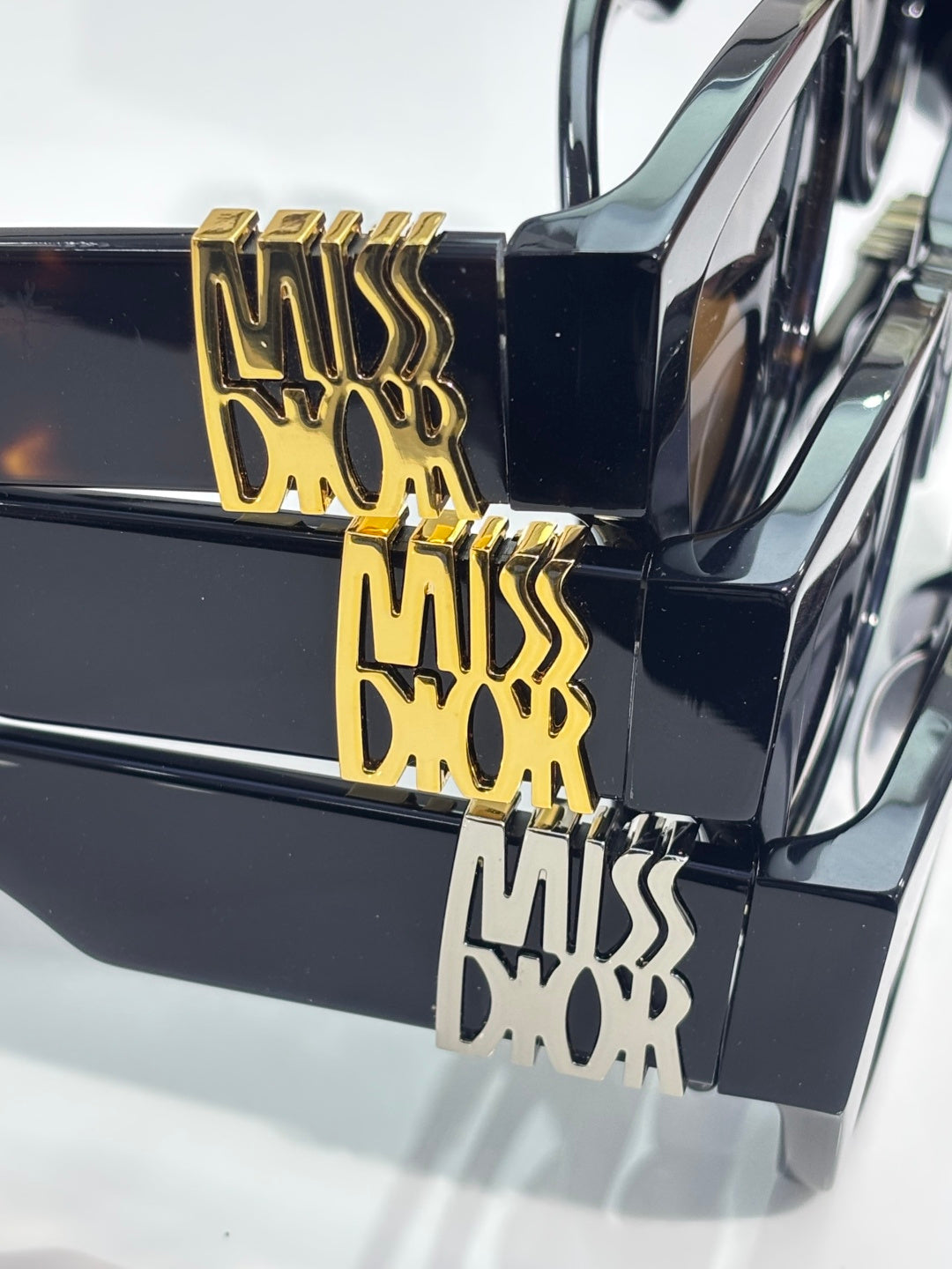 Close-up of gold logo plate on dark navy sunglasses temple, glossy frame