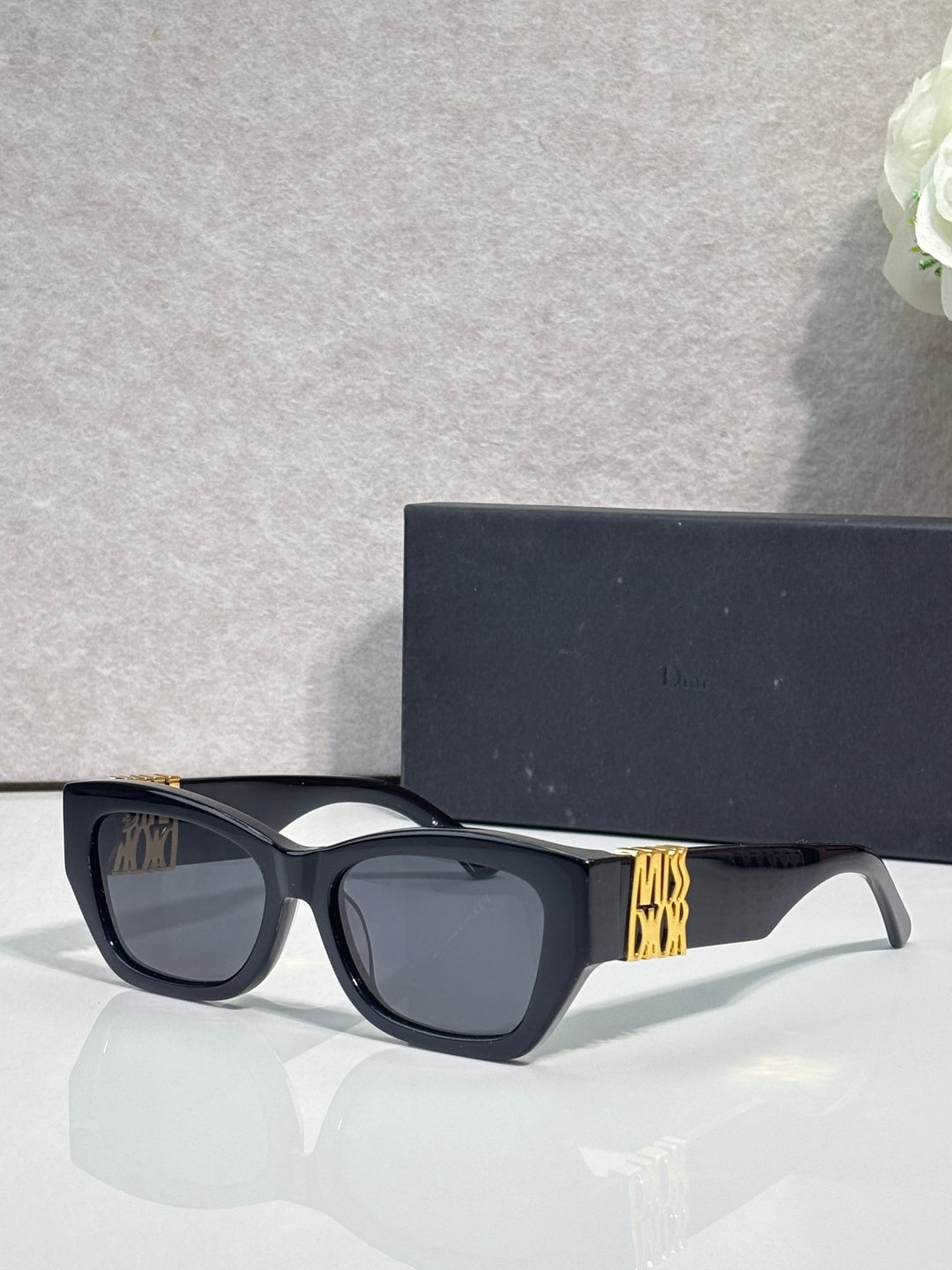 Sunglasses with dark navy cat-eye frames and gold geometric logo on temple, tinted lenses