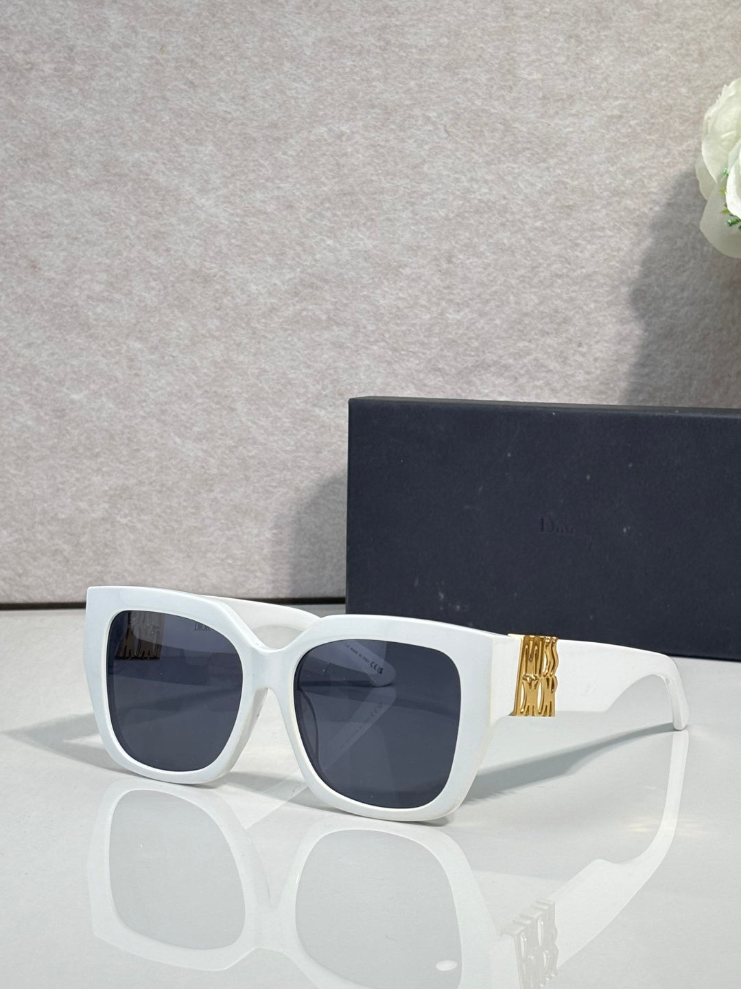 Dior sunglasses with white frames and dark lenses, gold logo detail on the temple