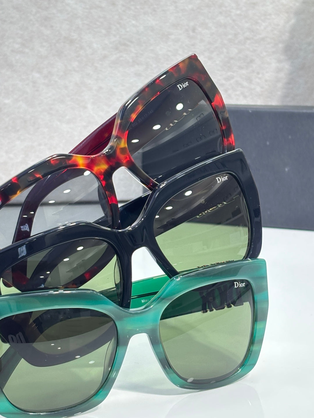 Stacked Dior glasses with green and tortoiseshell frames, gold temple lettering