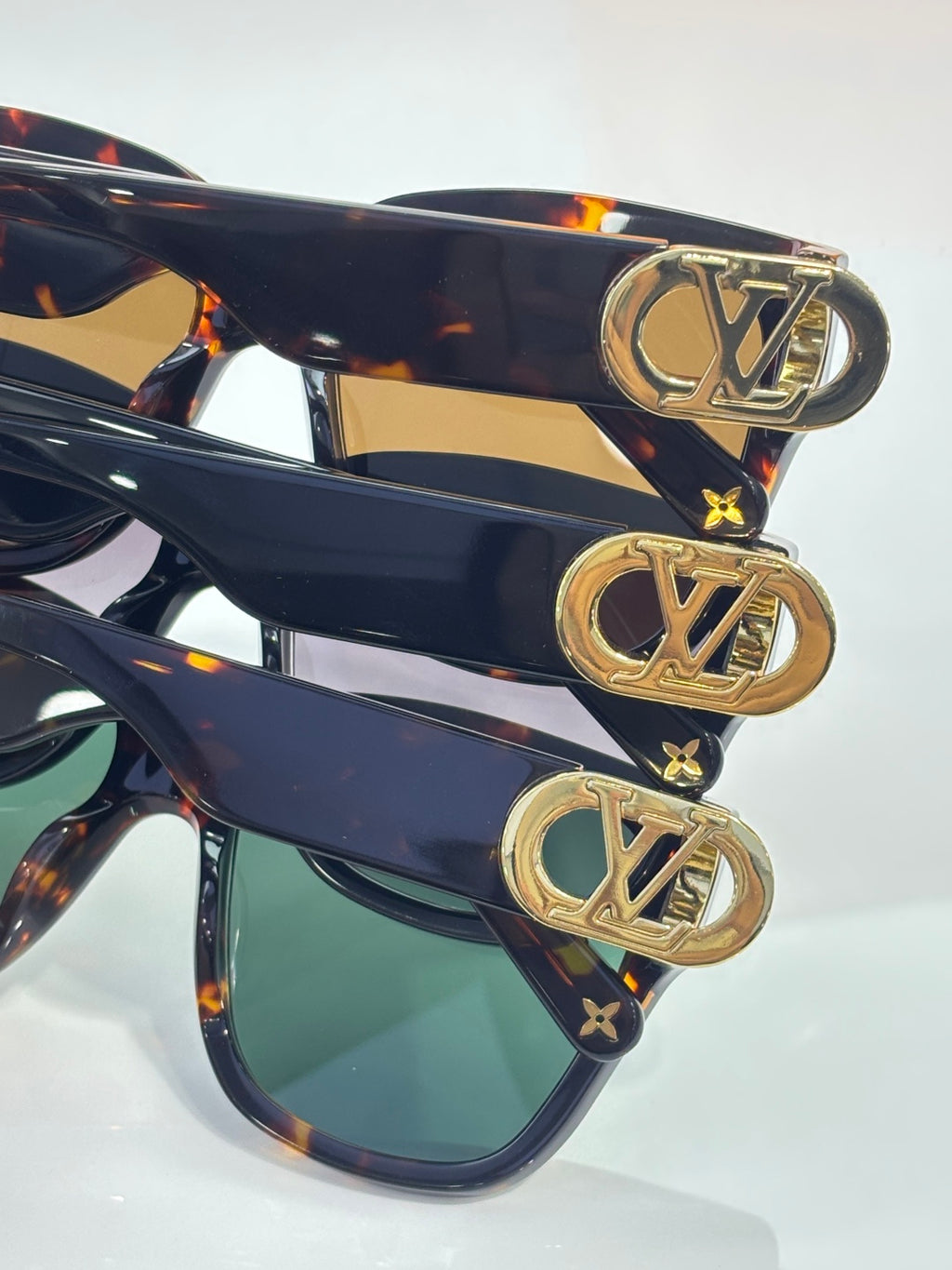 Sunglasses stack with dark frames, green lenses, and gold LV emblem hardware